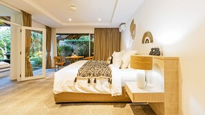 A modern bedroom with a large bed, a bedside table, and a view of a garden through a sliding door. - Baliani Beauty (Seminyak)