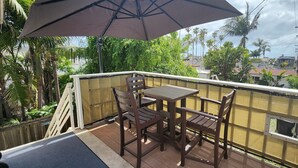 A balcony with a table and chairs, a large umbrella, and a view of palm trees and buildings.