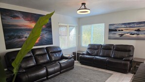 A living room with two black leather sofas, a large green plant, and two paintings on the walls.
