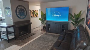 A living room with a fireplace, a large flat-screen TV displaying Disney+, a leather couch, and a coffee table.