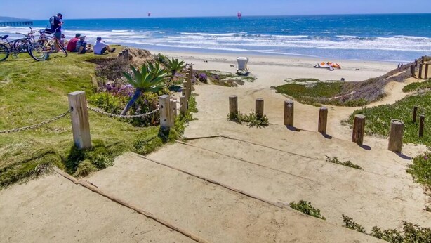 A beach pathway leading to the ocean with bicycles and people.