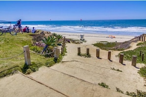 A beach pathway leading to the ocean with bicycles and people.