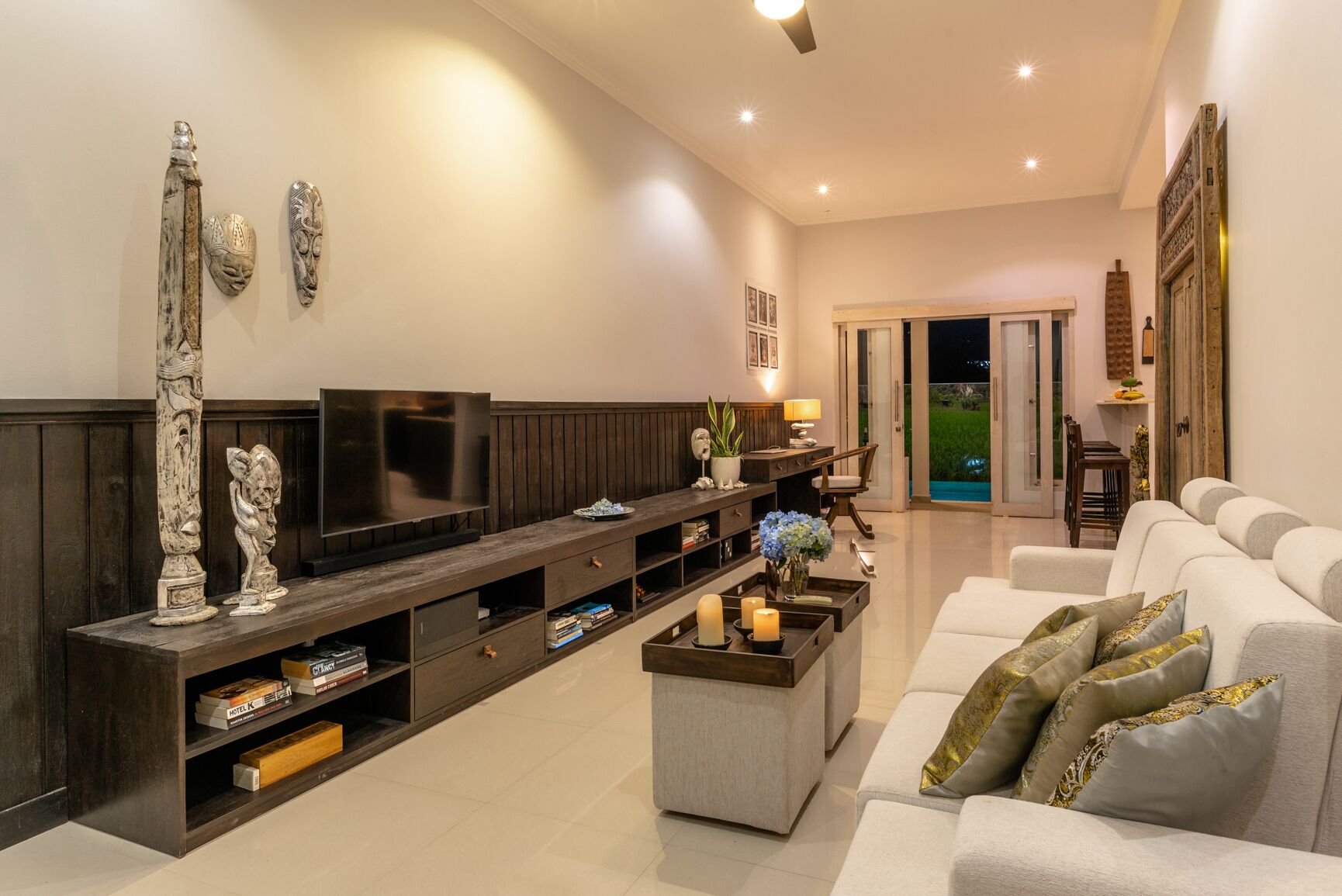 A modern living room with a flat-screen TV, a wooden entertainment unit, a grey coffee table, and a white sofa with decorative pillows.