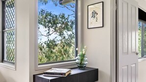 Ein Zimmer mit Fenster, einem gerahmten Bild an der Wand und einem kleinen Tisch mit Vase und Büchern.
