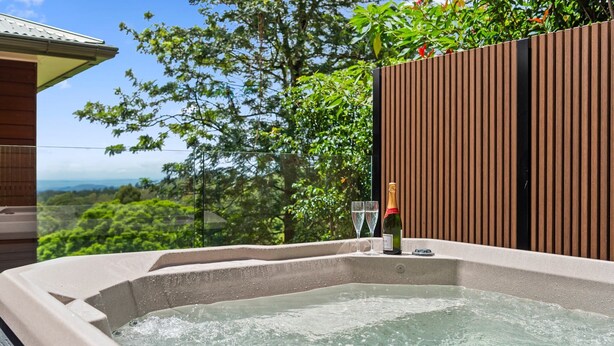 Ein Whirlpool mit Holzzaun und Glastüren, umgeben von Grünpflanzen und Blick auf die Landschaft.