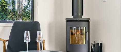 A modern room with a wood-burning stove, a round table with two glasses, and a chair.