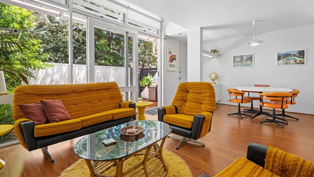 Ein modernes Wohnzimmer mit einer Couch, Sesseln, einem Glastisch und einem Essbereich mit rundem Tisch und Stühlen.