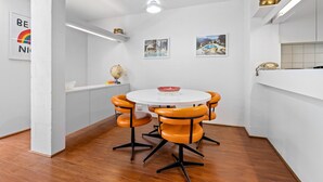 Eine moderne Küche mit weißen Schränken, einem runden Esstisch mit orangefarbenen Stühlen und einem weißen Deckenventilator.