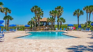 A pool area with lounge chairs and umbrellas, surrounded by palm trees. - Stunning First Floor Condo, Direct Beach Access! Two Pools, One Heated Pool, $300 in Free Tickets! (St. Augustine Beach)