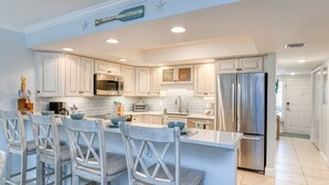 A modern kitchen with white cabinetry, stainless steel appliances, and a central island with bar stools. - Stunning First Floor Condo, Direct Beach Access! Two Pools, One Heated Pool, $300 in Free Tickets! (St. Augustine Beach)