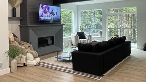 Ein modernes Wohnzimmer mit Kamin, Fernseher, Sofa und Blick ins Freie.