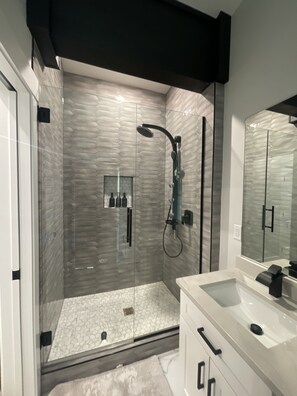 A modern bathroom with a glass-enclosed shower, a white vanity, and a large mirror. - 4th night FREE- Ski Condo with Hot Tub & Sauna (Girdwood)