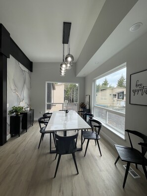 A modern dining area with a long table, black chairs, and a unique pendant light. - 4th night FREE- Ski Condo with Hot Tub & Sauna (Girdwood)