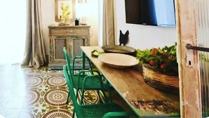 Un comedor con mesa de madera, sillas verdes, un televisor montado en la pared y un armario con espejo.