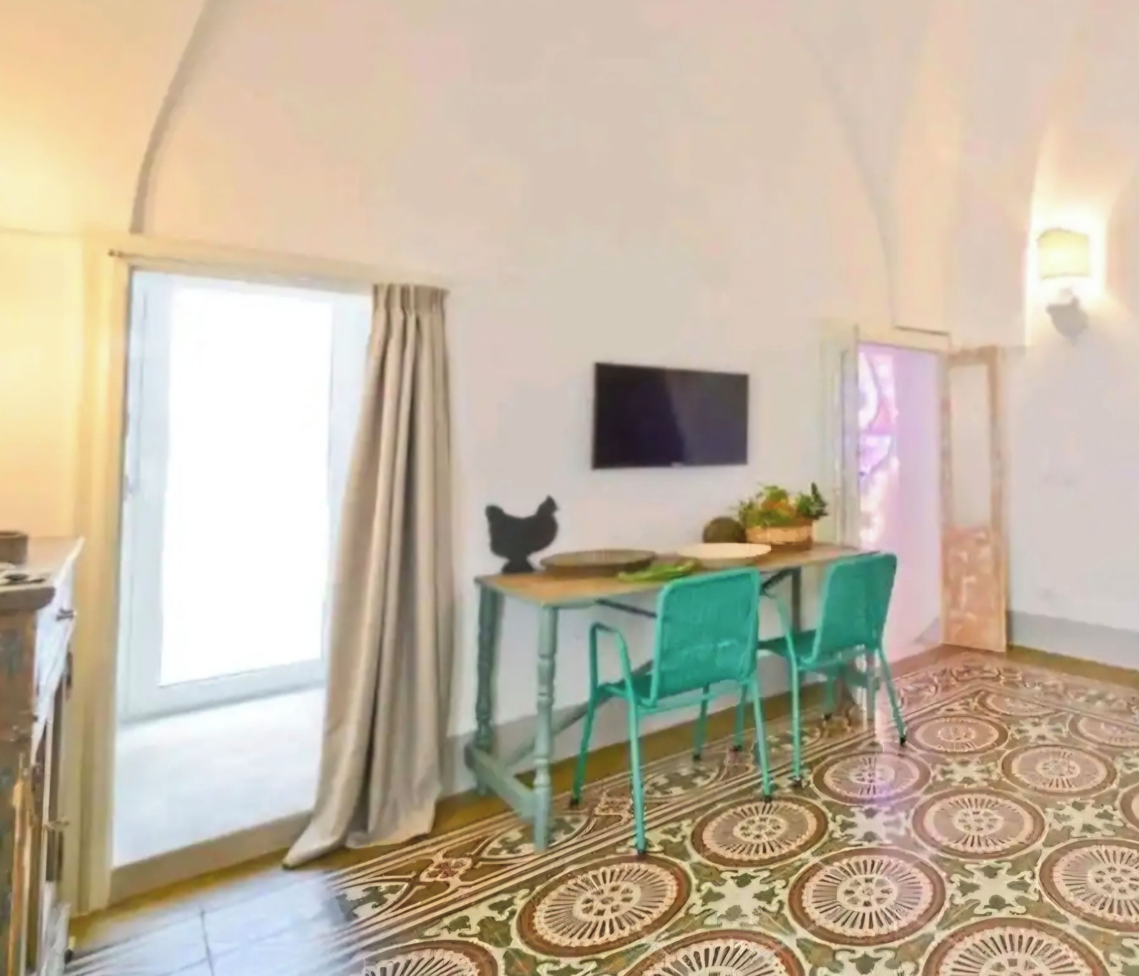 Una stanza con soffitto curvo, un tavolo da pranzo con sedie, una TV a schermo piatto e un pavimento decorato.