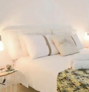 Un lit avec une literie blanche et un couvre-lit à motifs, une table de chevet avec une lampe et une étagère fixée au mur.