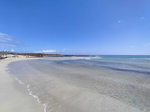 A beach with clear water, a sandy shore, and a rocky breakwater in the background. - L'Angolo di Ostuni (Ostuni)