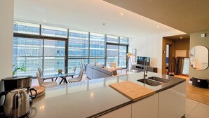 Eine moderne Küche mit einer großen Kochinsel, einem Essbereich mit einem Glastisch und einem Wohnbereich mit Sofa und Fernseher.