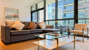 Ein modernes Wohnzimmer mit einem Ecksofa, einem Glastisch und Blick auf ein Hochhaus.