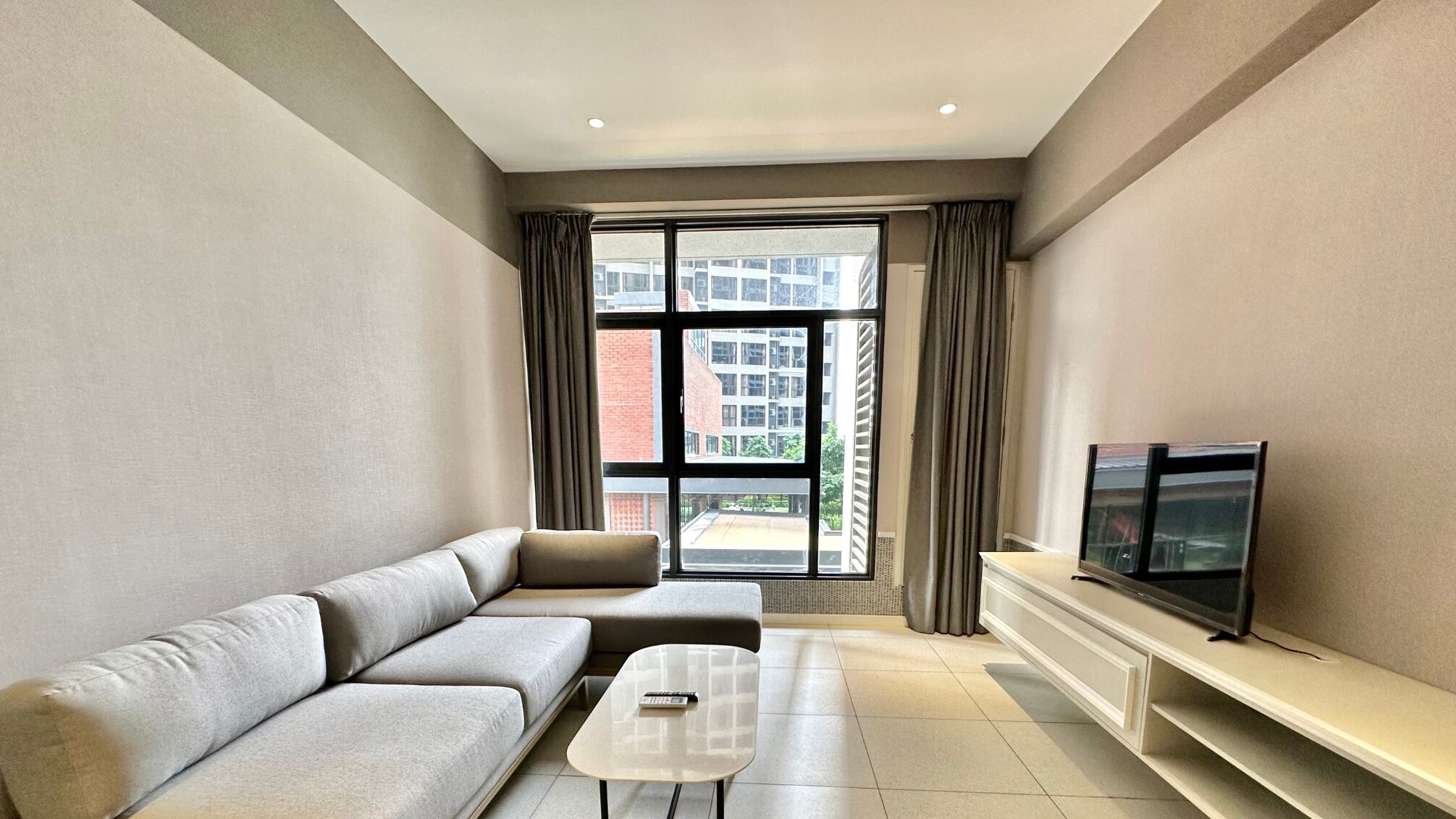 Una sala de estar moderna con un sofá gris, una mesita de centro y un televisor sobre un mueble blanco.