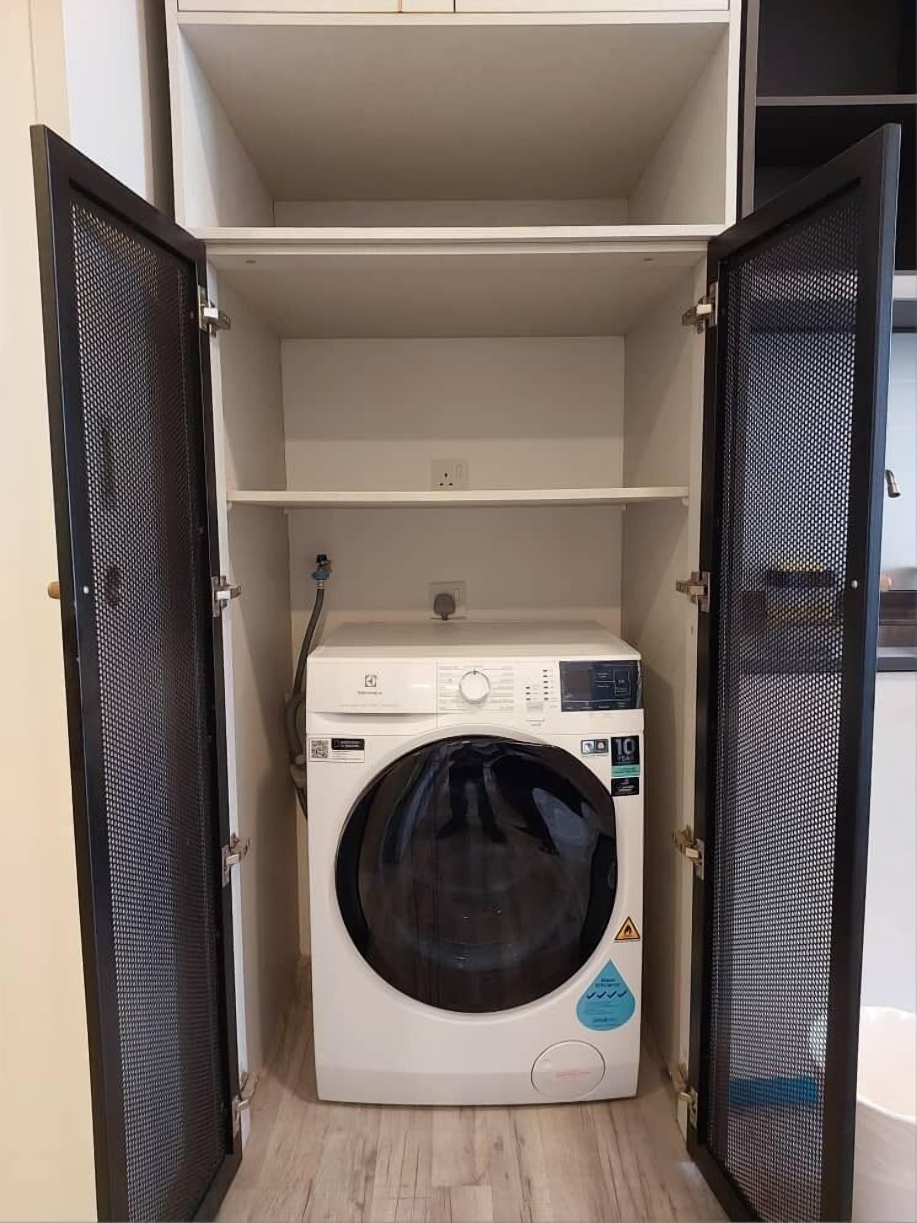 A compact, white washing machine in a small, enclosed laundry room with open doors and a wooden floor.