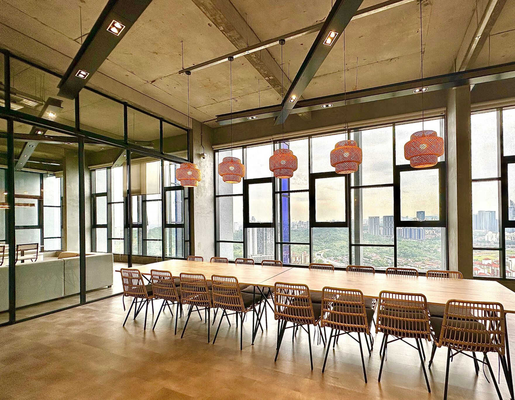 Een ruime vergaderzaal met een lange tafel en rieten stoelen, grote ramen met uitzicht op de stad, en hangende oranje lampen.