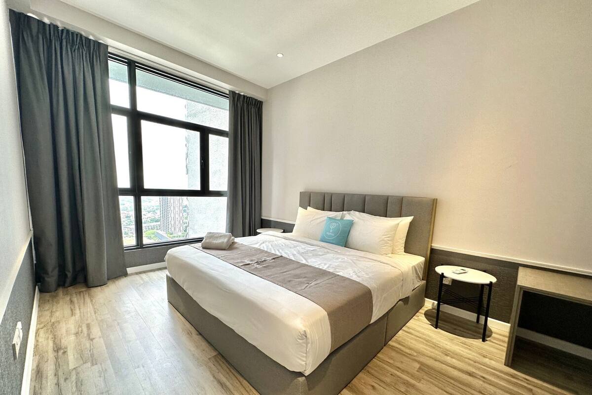 Una habitación de hotel moderna con una cama grande, una mesita de noche pequeña y vistas a la ciudad a través de la ventana.