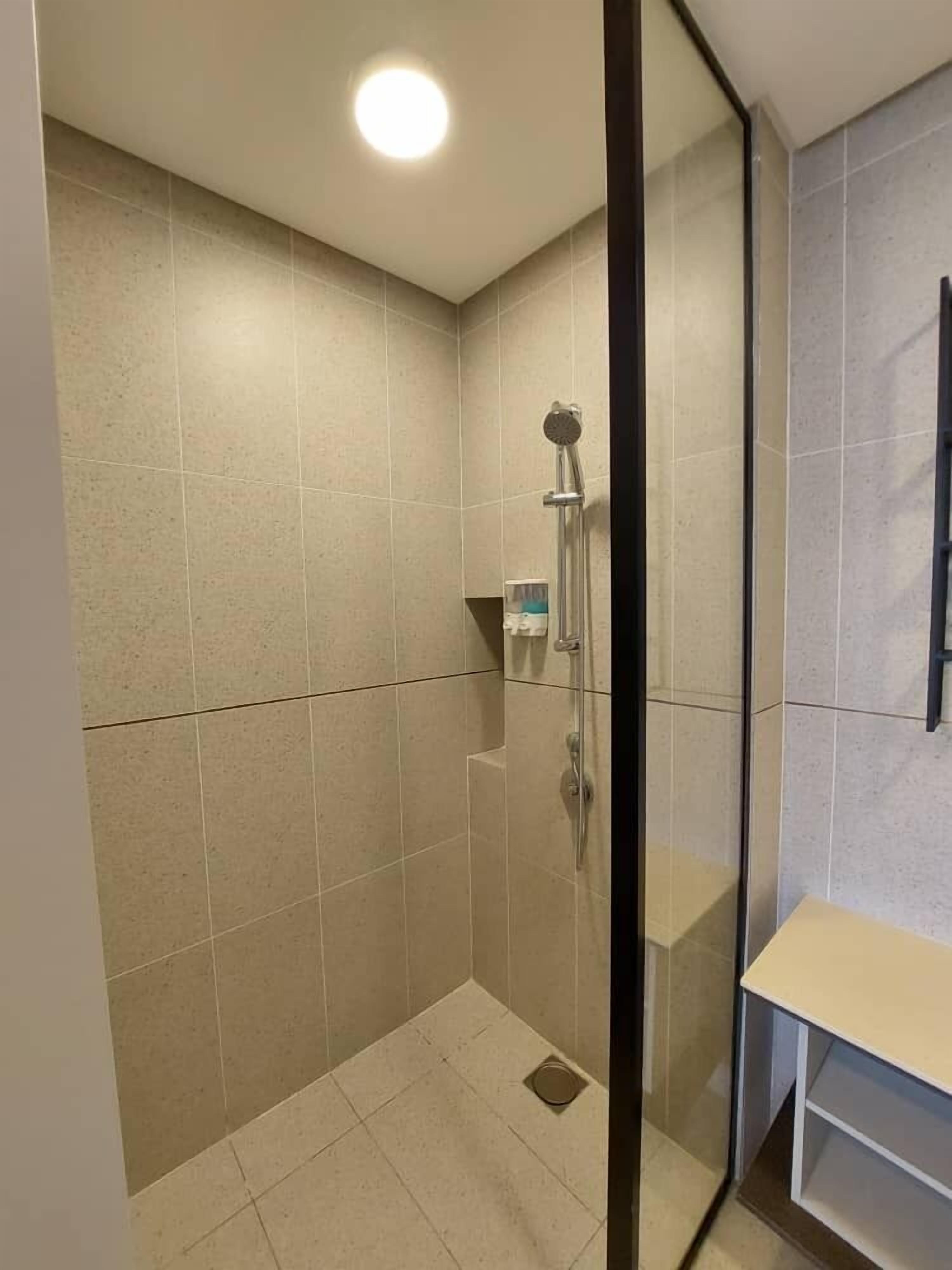 Een moderne badkamer met een douchecabine van glas, betegelde wanden en een klein plankje met toiletartikelen.