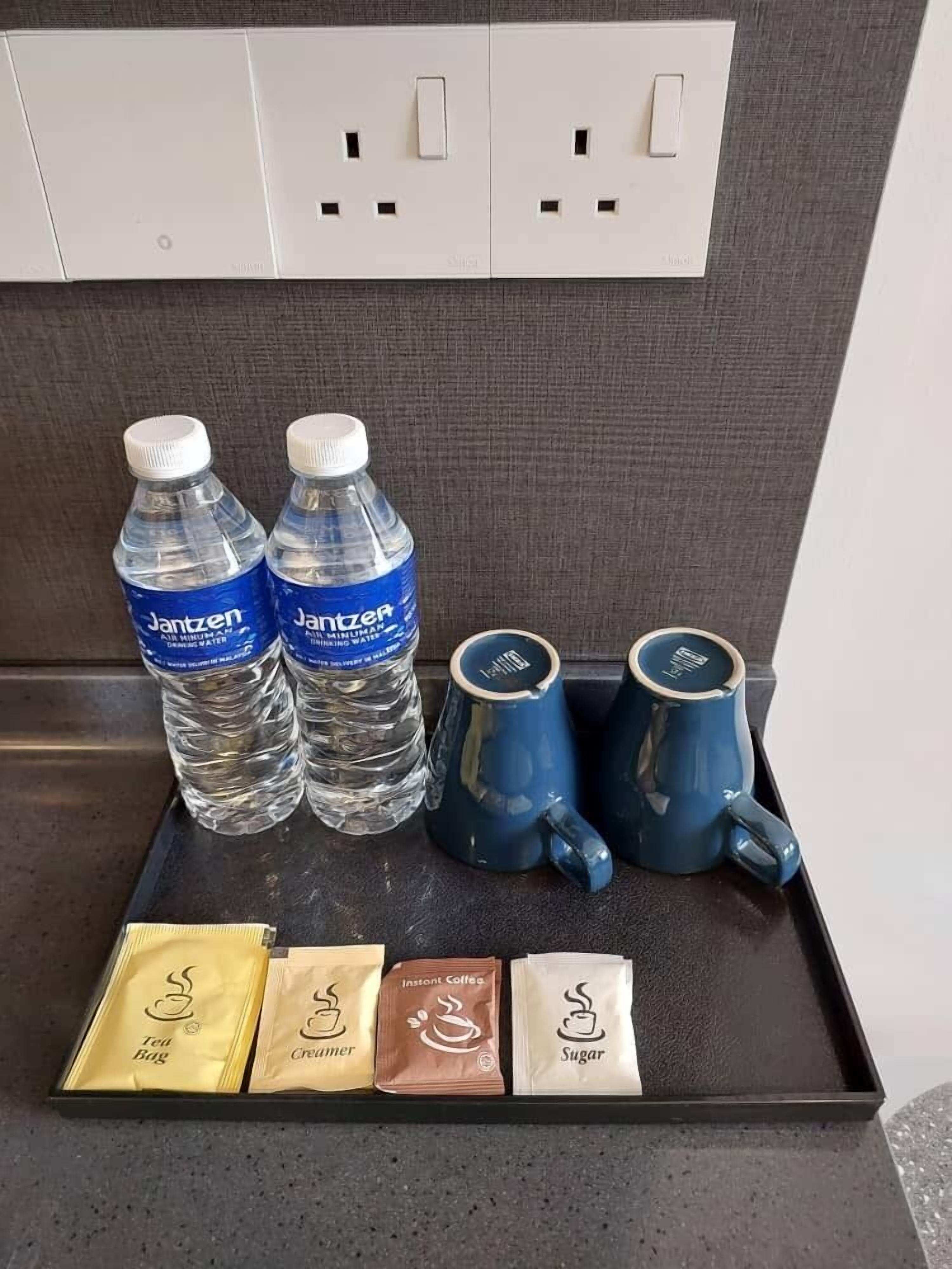 A tray with water bottles, mugs, tea bags, creamer, instant coffee, and sugar packets.