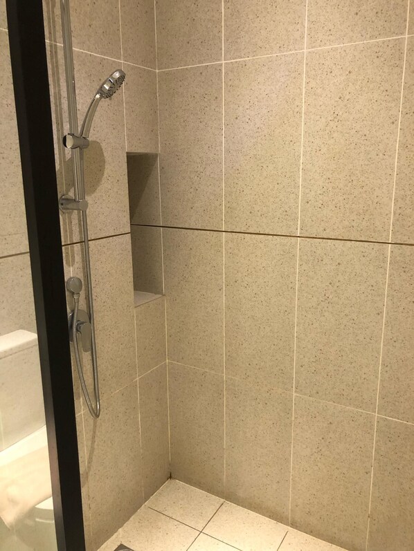 A shower with a handheld showerhead, a wall-mounted faucet, and a small shelf.