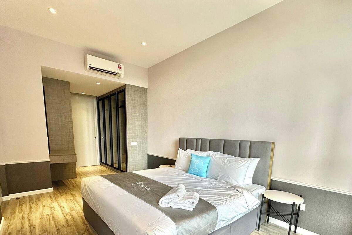 Una habitación de hotel moderna con una cama grande, una mesita de noche pequeña, un equipo de aire acondicionado y vistas a un pasillo.