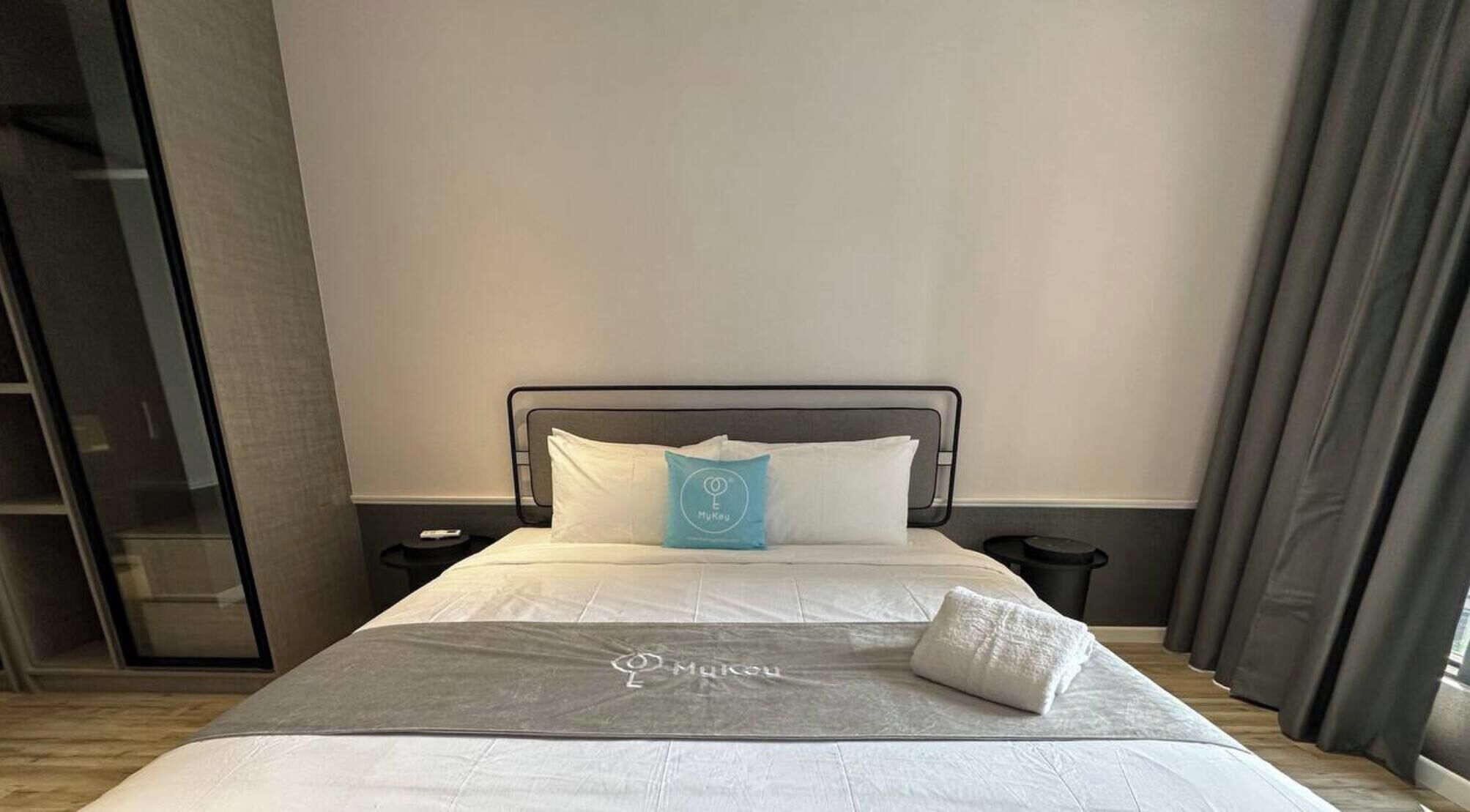 A hotel room with a bed, a nightstand, a remote control, and a window with curtains.