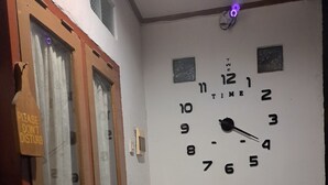 Una habitación con un reloj de pared, una puerta con un cartel de 'No molestar' y dos sillas de madera con un cojín verde.