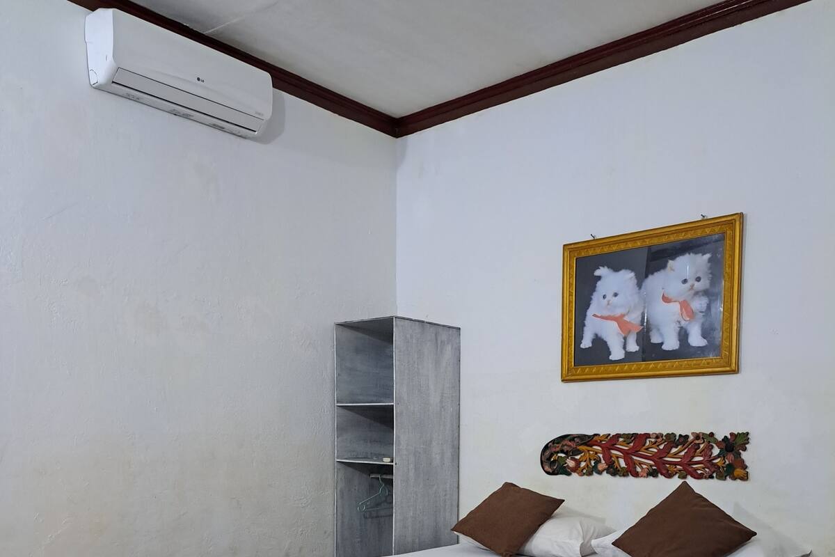 A bedroom with a bed, pillows, a wardrobe, an air conditioner, and a wall decoration.