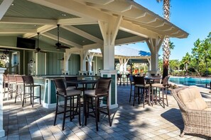 A covered outdoor area with a bar, seating, and a pool.