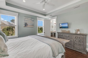 Een slaapkamer met een groot bed, een dressoir, een televisie en uitzicht op het omliggende landschap.