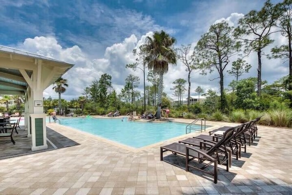 A pool area with lounge chairs, a covered seating area, and surrounding trees.