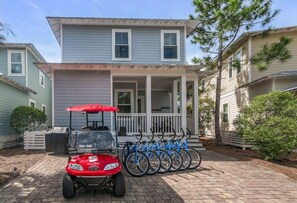 Une maison à deux étages avec un porche, un petit véhicule de golf rouge et une rangée de vélos.
