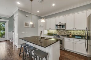 A kitchen with white cabinets, a large island with stools, stainless steel appliances, and pendant lighting.