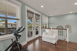 A room with a white sofa, a stationary bike, and a view of a balcony. - Golf Cart & 6 Bikes! 2 King Suites! - Beckoning Breeze at NatureWalk on 30A (Santa Rosa Beach)