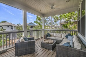 A covered porch with wicker furniture, a ceiling fan, and a view of neighboring houses and trees.
