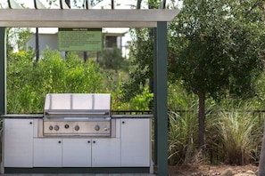 Un barbecue extérieur, agrémenté d’un panneau indiquant les règles d’utilisation, et entouré de verdure.