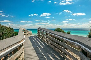 Een houten looppad dat naar een strand leidt, met helder turquoise water en een heldere lucht.
