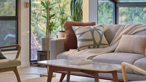 A modern living room with a sofa, coffee table, and floor lamp. There are large windows and a view of greenery outside. - Mid-Century Home in the Heart of Sedona (Sedona)