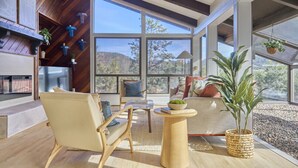 A modern living room with a large window, a wooden ceiling, and a stone fireplace. - Mid-Century Home in the Heart of Sedona (Sedona)