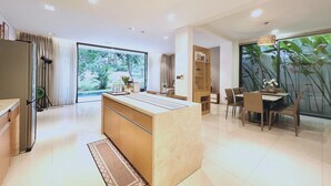 A modern kitchen with a central island, a dining area with chairs and a table, and a large window with a view of greenery.