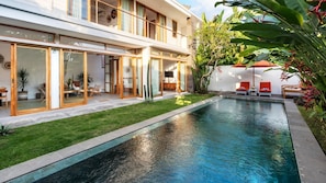 Uma casa moderna com dois andares, piscina, portas de vidro e área de varanda com móveis para área externa.