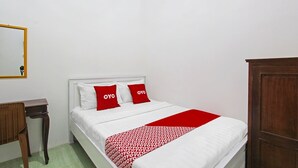Een net opgemaakt bed met wit beddengoed en rode kussens, een houten nachtkastje en een houten garderobe.