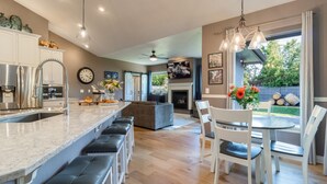 A modern kitchen with a central island, bar stools, and a dining area with white chairs. - Welcome to The Greentree Retreat (Walla Walla)