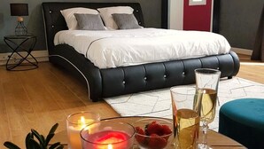 A modern bedroom with a black upholstered bed, white bedding, a bedside table with a lamp, and a small potted plant. - Chateau de la Rose (Cluis)